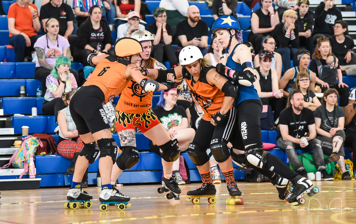 Three Tiger Bay Brawlers blockers playing roller derby against an opposing teams jammer at a public game